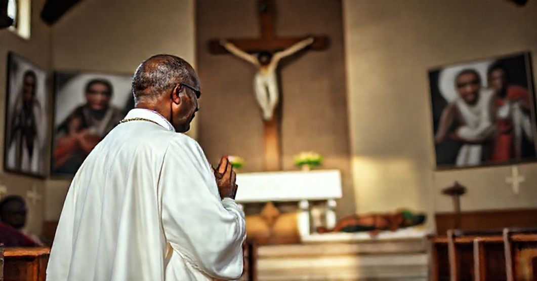 A Catholic priest praying in a Nigerian church amidst images of martyrs, highlighting the persecution of Christians and the need for Christ's social reign.