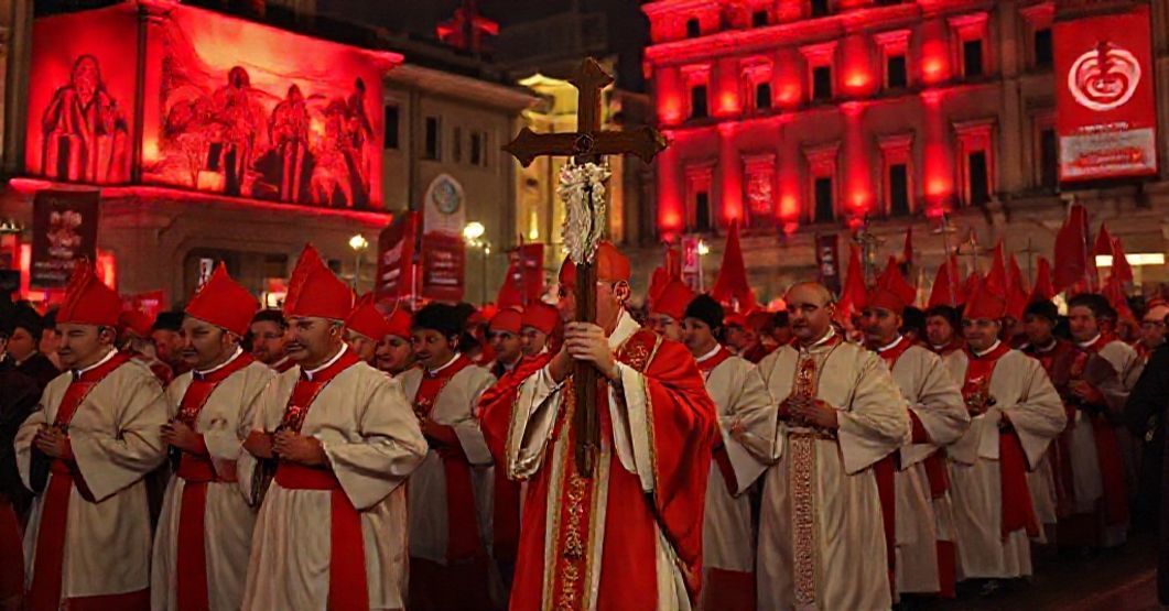 A Catholic bishop leads a traditional procession under red-lit buildings during 'Red Week 2025,' symbolizing the clash between true martyrdom and modernist activism.