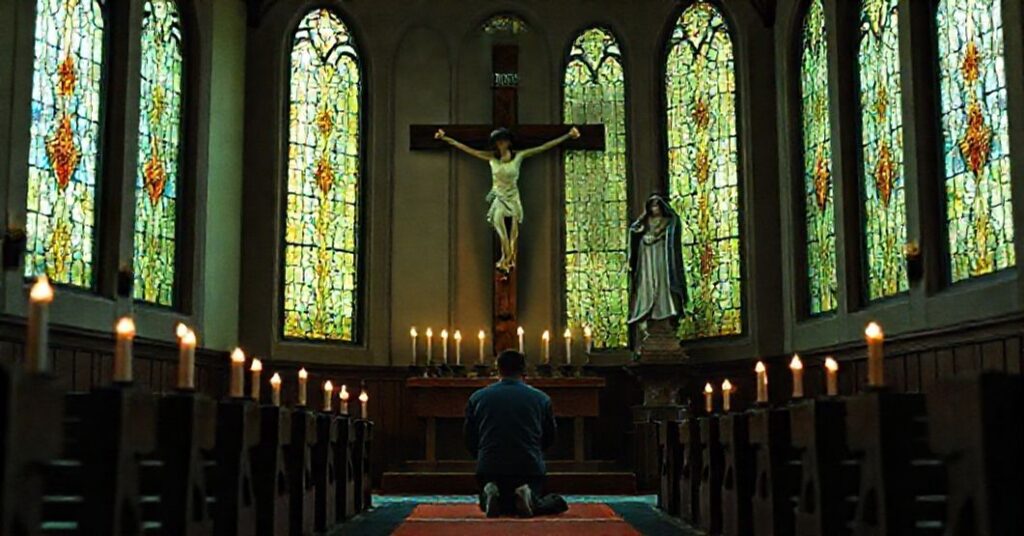A Catholic worshiper kneeling in prayer before a wooden crucifix in a traditional church setting.